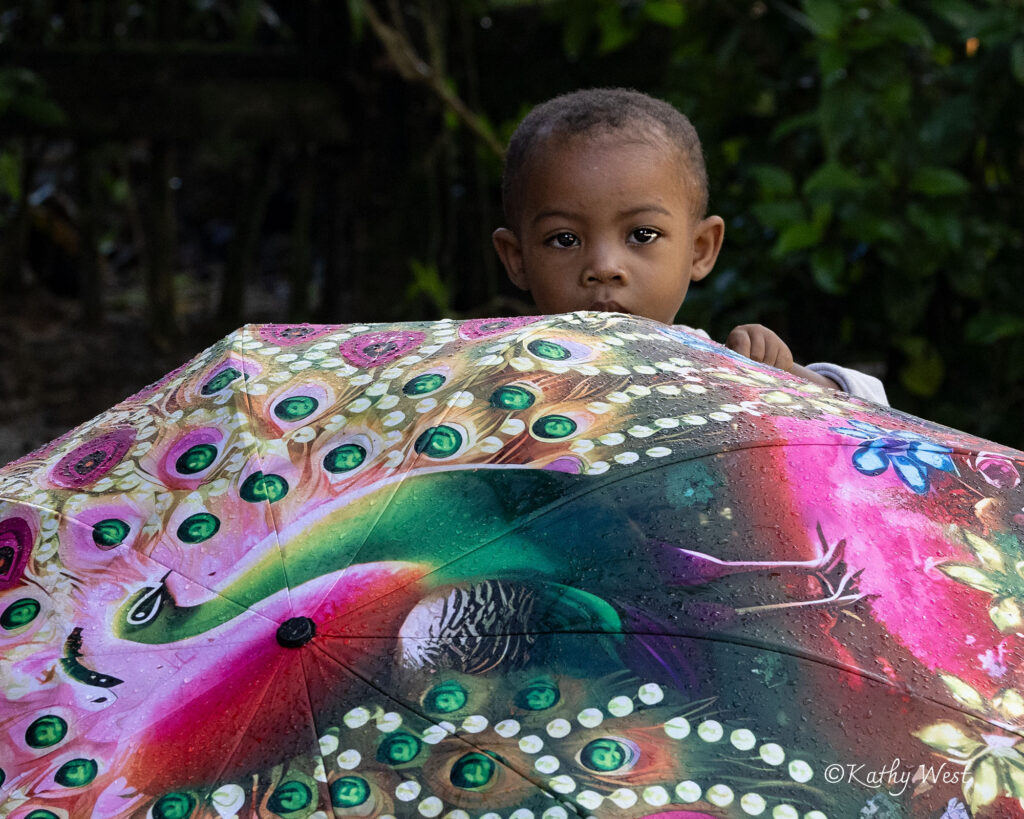 a small child peeks out from behind a colorful umbrella
